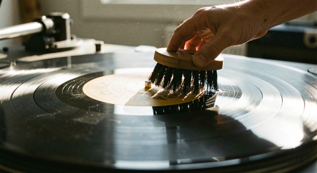 Brosse antistatique passée sur un vinyle en rotation, poils frôlant les sillons sous une lumière rasante.